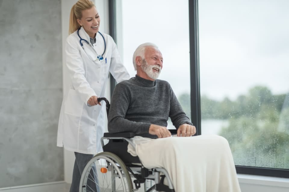Ärztin begleitet einen älteren Patienten im Rollstuhl